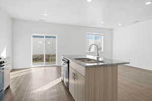 Kitchen featuring dark stone countertops, dark wood-type flooring, a center island with sink, stainless steel appliances, and recessed lighting