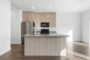 Kitchen featuring dark wood-type flooring, a center island with sink, light stone countertops, black appliances, and light wood finish cabinets