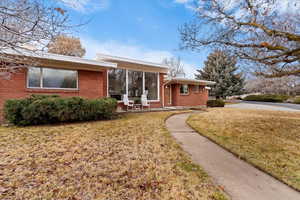View of front of house with a front yard, brick siding, and a sunroom
