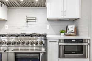 Kitchen with stainless steel appliances, white cabinetry, and light stone counters