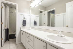 Bathroom featuring double vanity, shower / bathtub combination with curtain, and light tile patterned floors