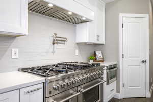Kitchen featuring double oven range, white cabinets, light stone counters, and backsplash