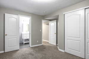 Unfurnished bedroom featuring carpet, a closet, ensuite bathroom, and a textured ceiling