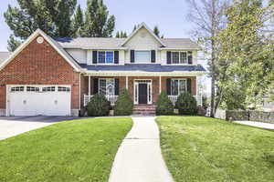 Traditional home with covered porch, roof with shingles, driveway, brick siding, and a garage