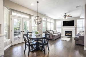 Dining room featuring dark wood-style flooring, a fireplace with flush hearth, suspended lighting, ceiling fan, and french doors