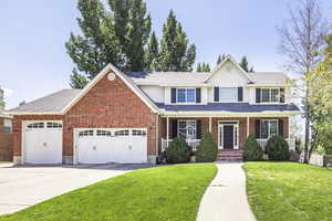 Traditional home with a front lawn, covered porch, driveway, a garage, and brick siding