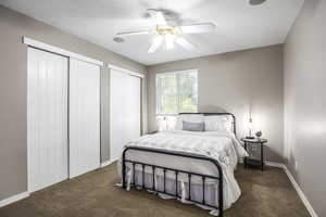 Bedroom with two closets, a ceiling fan, dark carpet, and a textured ceiling