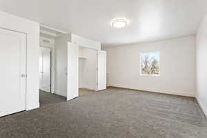 Unfurnished bedroom with dark colored carpet and baseboards