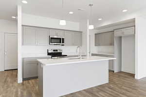 Kitchen with gray cabinetry, hanging light fixtures, stainless steel appliances, and light wood-style floors