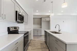 Kitchen featuring gray cabinets, stainless steel appliances, hanging light fixtures, and light wood-style floors