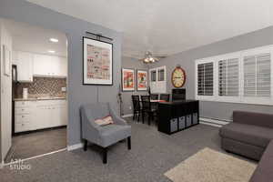 Living area featuring dark colored carpet, a baseboard heating unit, a ceiling fan, and recessed lighting