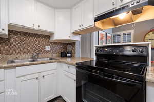 Kitchen featuring black / electric stove, white cabinetry, light stone counters, and tasteful backsplash