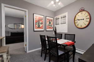 Dining room with dark colored carpet, baseboard heating, and a ceiling fan