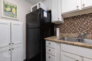 Kitchen with white cabinetry, freestanding refrigerator, tasteful backsplash, and light stone counters