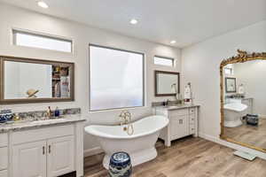 Bathroom with a soaking tub, light wood finished floors, two vanities, and recessed lighting