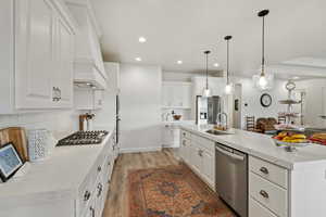 Kitchen featuring white cabinetry, stainless steel appliances, decorative light fixtures, and light wood-style floors