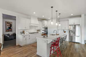 Kitchen featuring stainless steel appliances, a kitchen bar, hanging light fixtures, white cabinets, and a kitchen island with sink