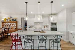 Kitchen featuring tasteful backsplash, stainless steel appliances, a kitchen island with sink, light wood-style floors, and white cabinetry