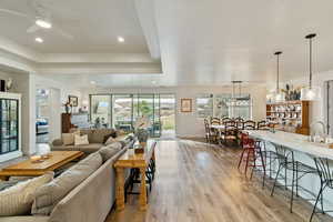 Living area featuring light wood finished floors, a raised ceiling, ceiling fan, and recessed lighting
