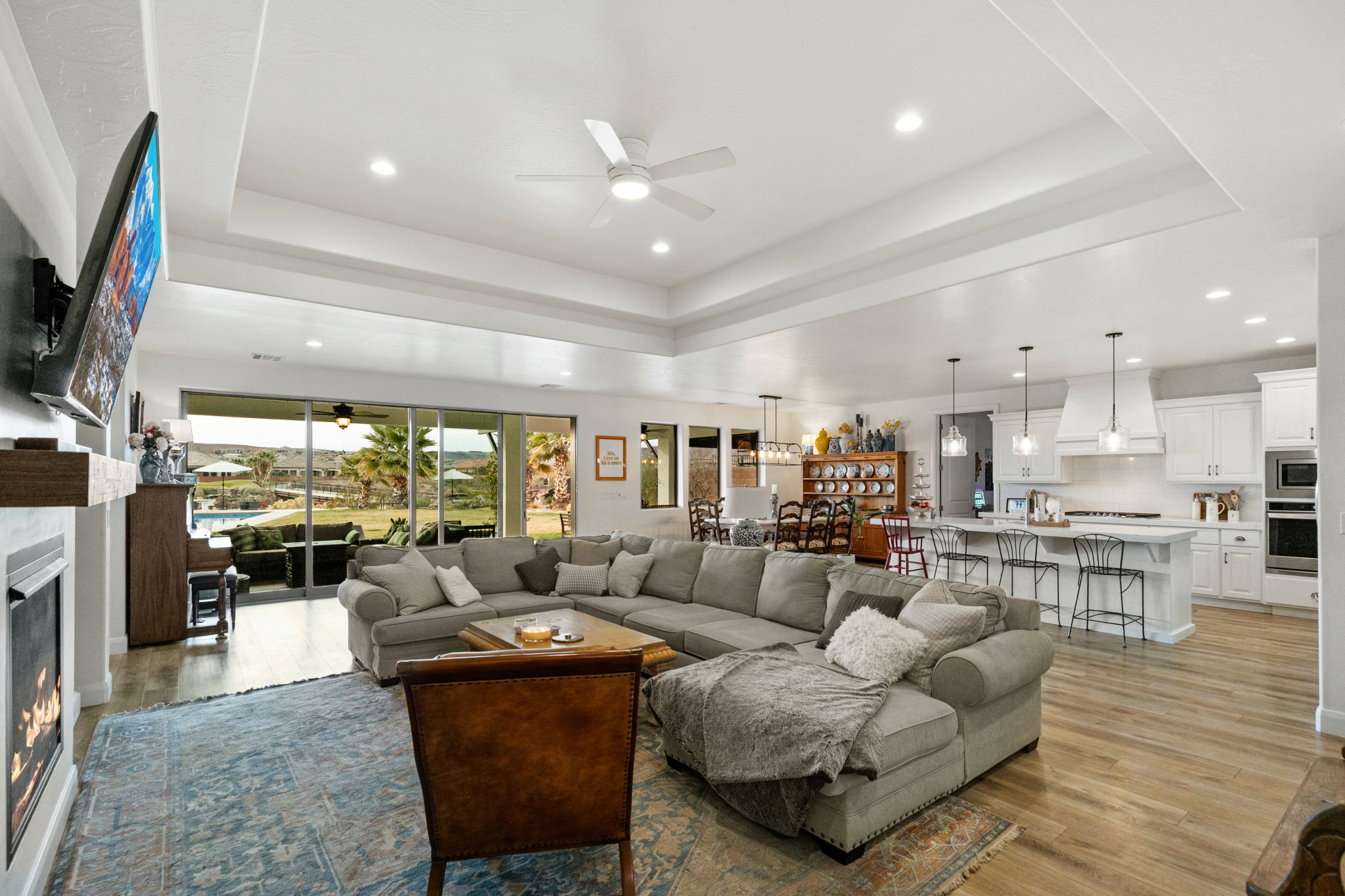 Living area featuring a ceiling fan, recessed lighting, light wood-style floors, a glass covered fireplace, and a tray ceiling