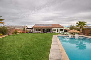 Rear view of house with outdoor dining space, roof mounted solar panels, a patio area, a tiled roof, and a fenced backyard
