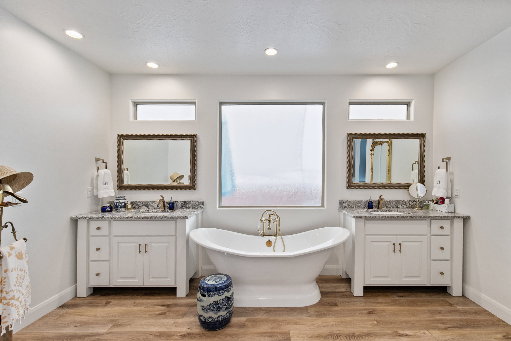 Bathroom featuring light wood finished floors, a freestanding tub, two vanities, plenty of natural light, and recessed lighting