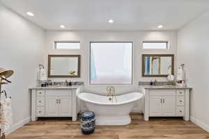 Bathroom featuring light wood finished floors, a freestanding tub, two vanities, plenty of natural light, and recessed lighting