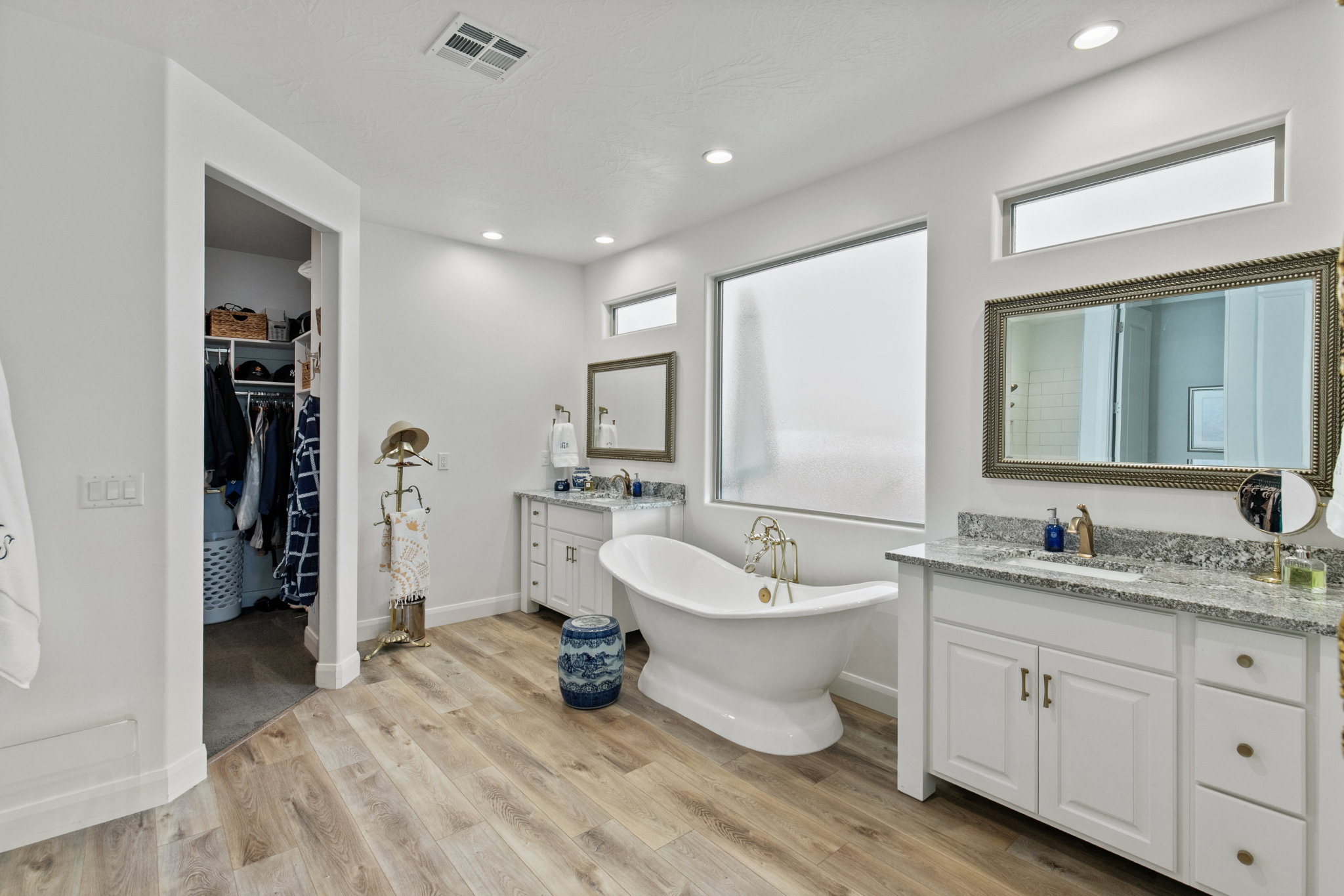 Bathroom with two vanities, a walk in closet, a freestanding tub, light wood-style floors, and plenty of natural light