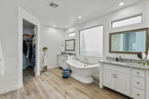 Bathroom with two vanities, a walk in closet, a freestanding tub, light wood-style floors, and plenty of natural light