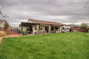 Back of house with solar panels, a ceiling fan, a patio, an outdoor living / dining area, and a fenced backyard
