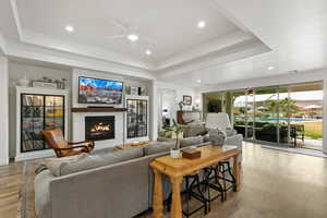 Living area with a ceiling fan, recessed lighting, light wood-style floors, a lit fireplace, and a raised ceiling