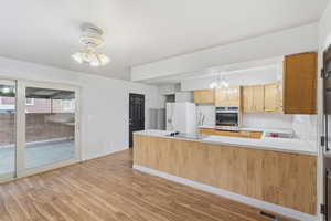 Kitchen featuring light countertops, a peninsula, light wood-type flooring, white fridge with ice dispenser, and stainless steel oven