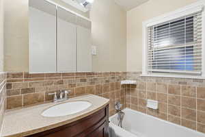 Bathroom featuring a textured wall, vanity, and a garden tub