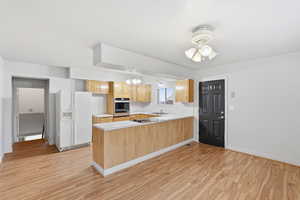 Kitchen with light countertops, white refrigerator with ice dispenser, light wood-style flooring, suspended lighting, and a peninsula
