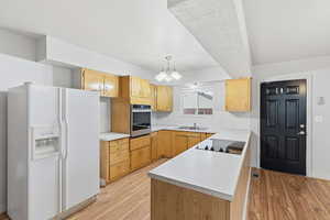 Kitchen with white fridge with ice dispenser, light countertops, a peninsula, stainless steel oven, and light wood-style floors