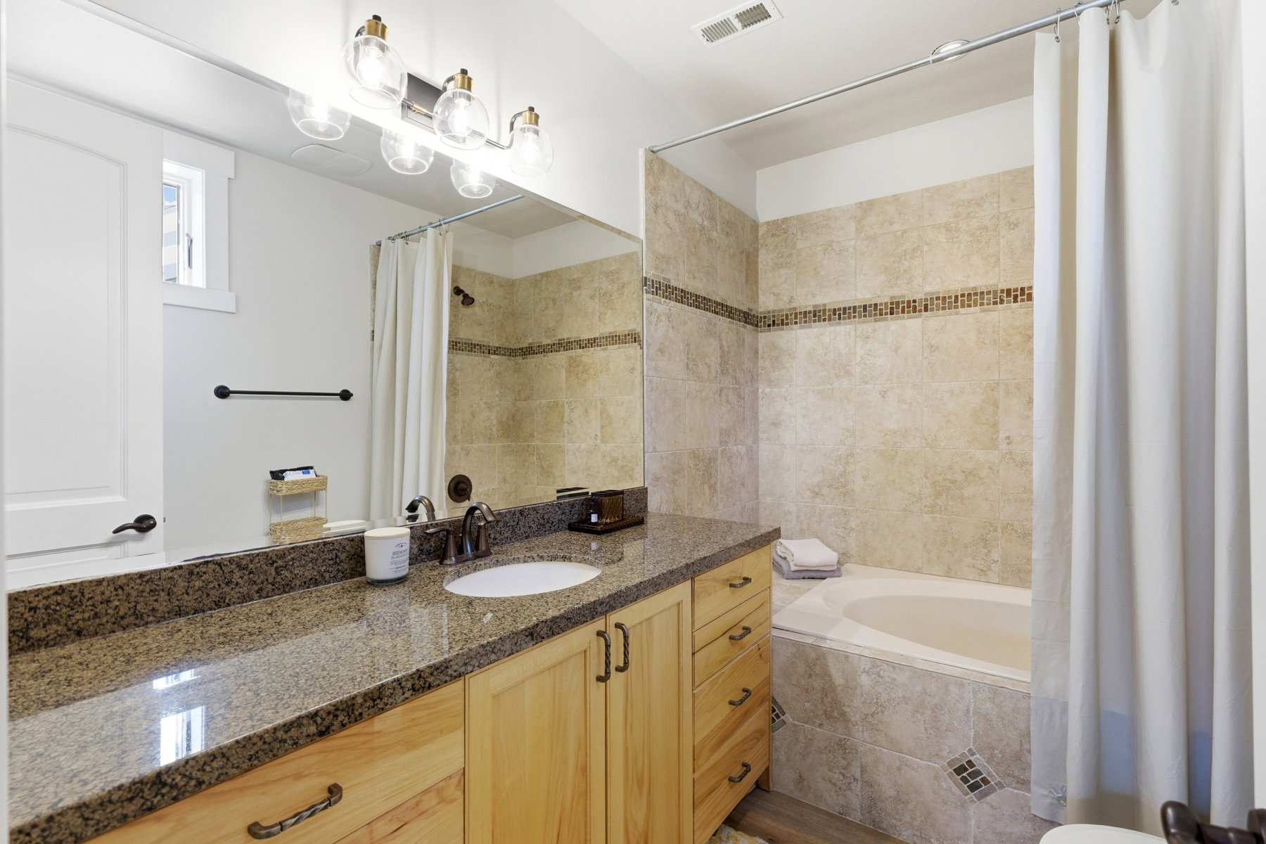 Bathroom featuring a light wood vanity with a granite countertop and an undermount sink