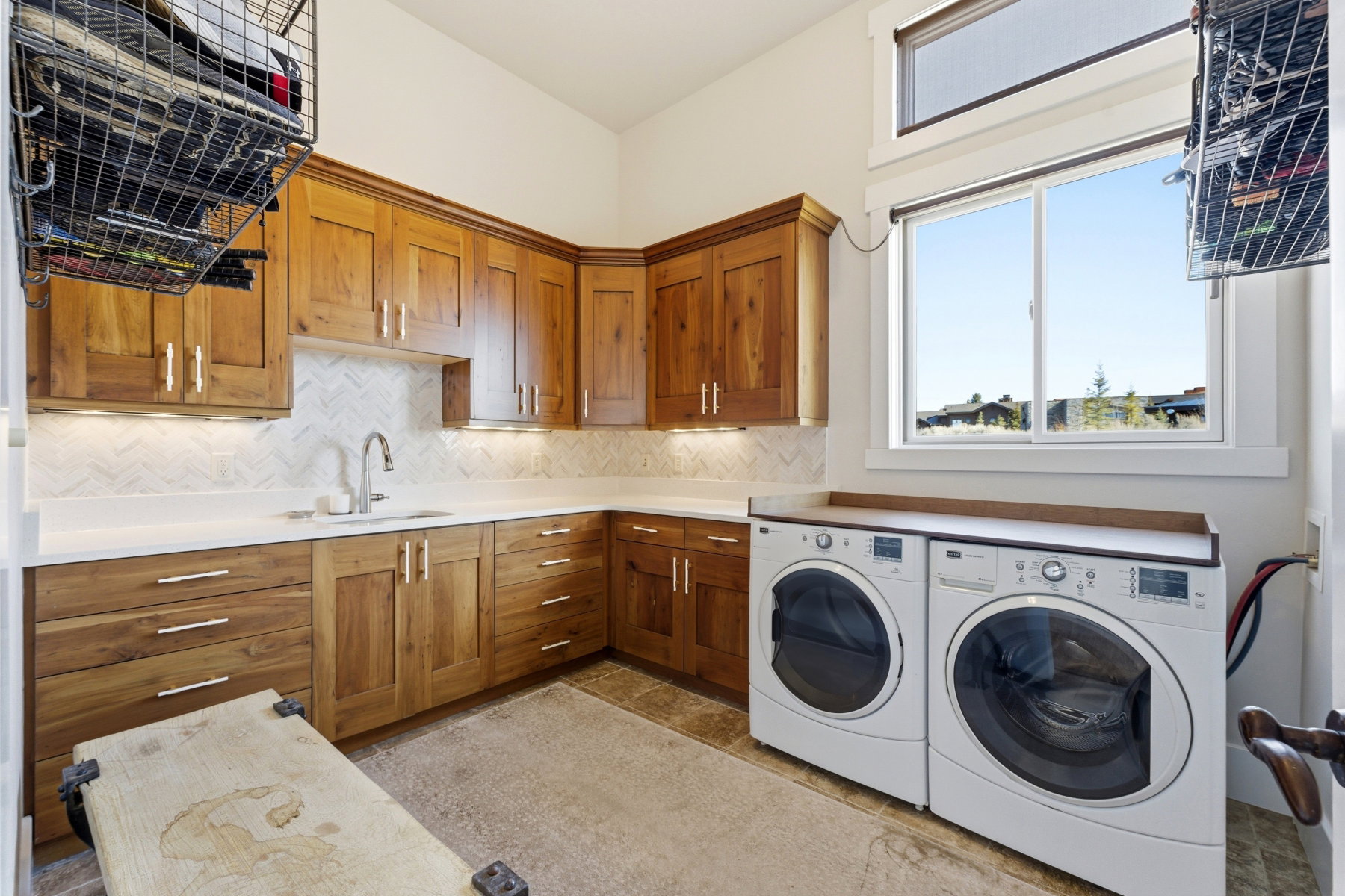 Laundry room featuring wood cabinetry, white countertops, a herringbone tile backsplash, and a sink with a gooseneck faucet