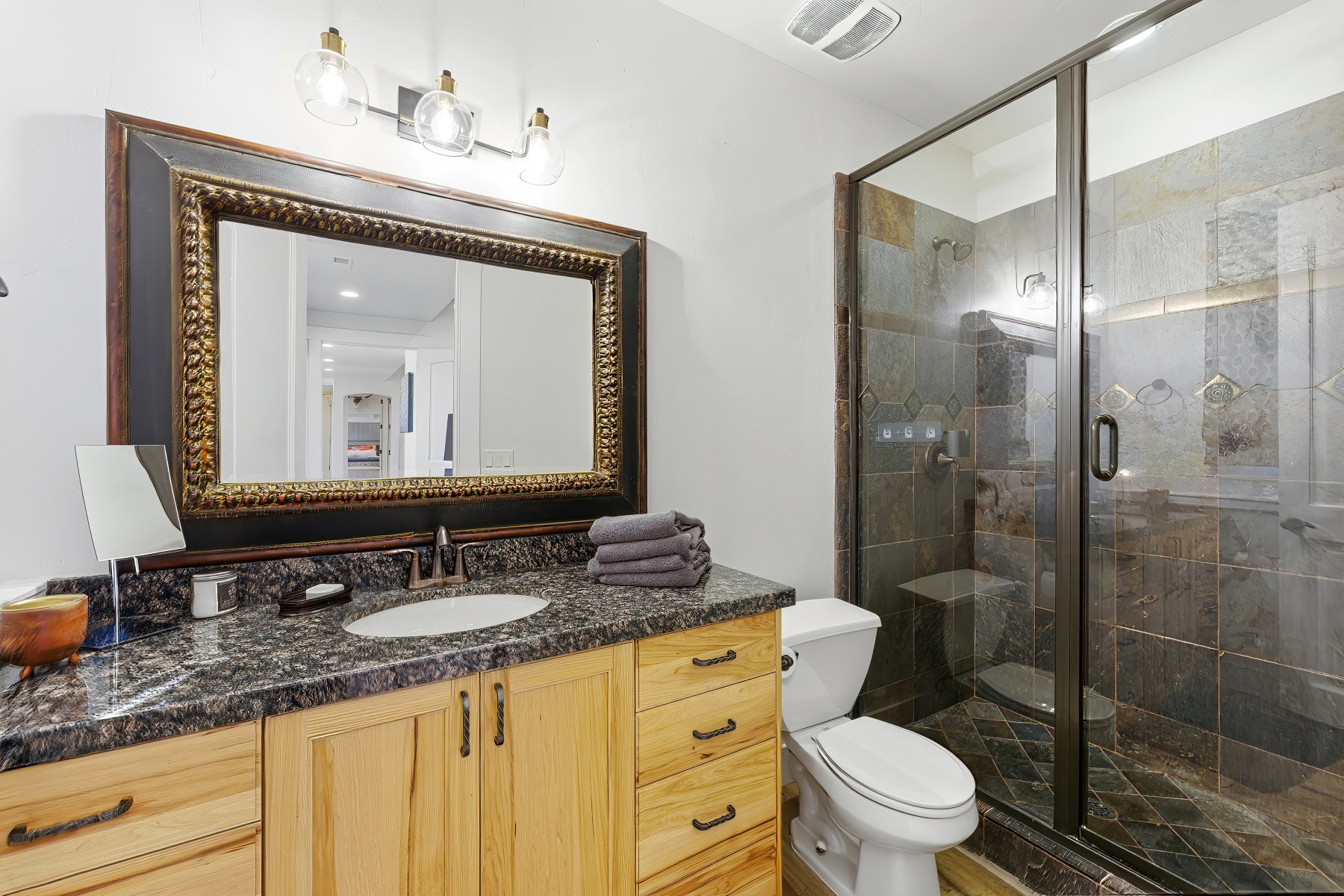 Bathroom featuring a custom wood vanity with a stone countertop, an ornate framed mirror, and a glass-enclosed shower with natural stone tile work