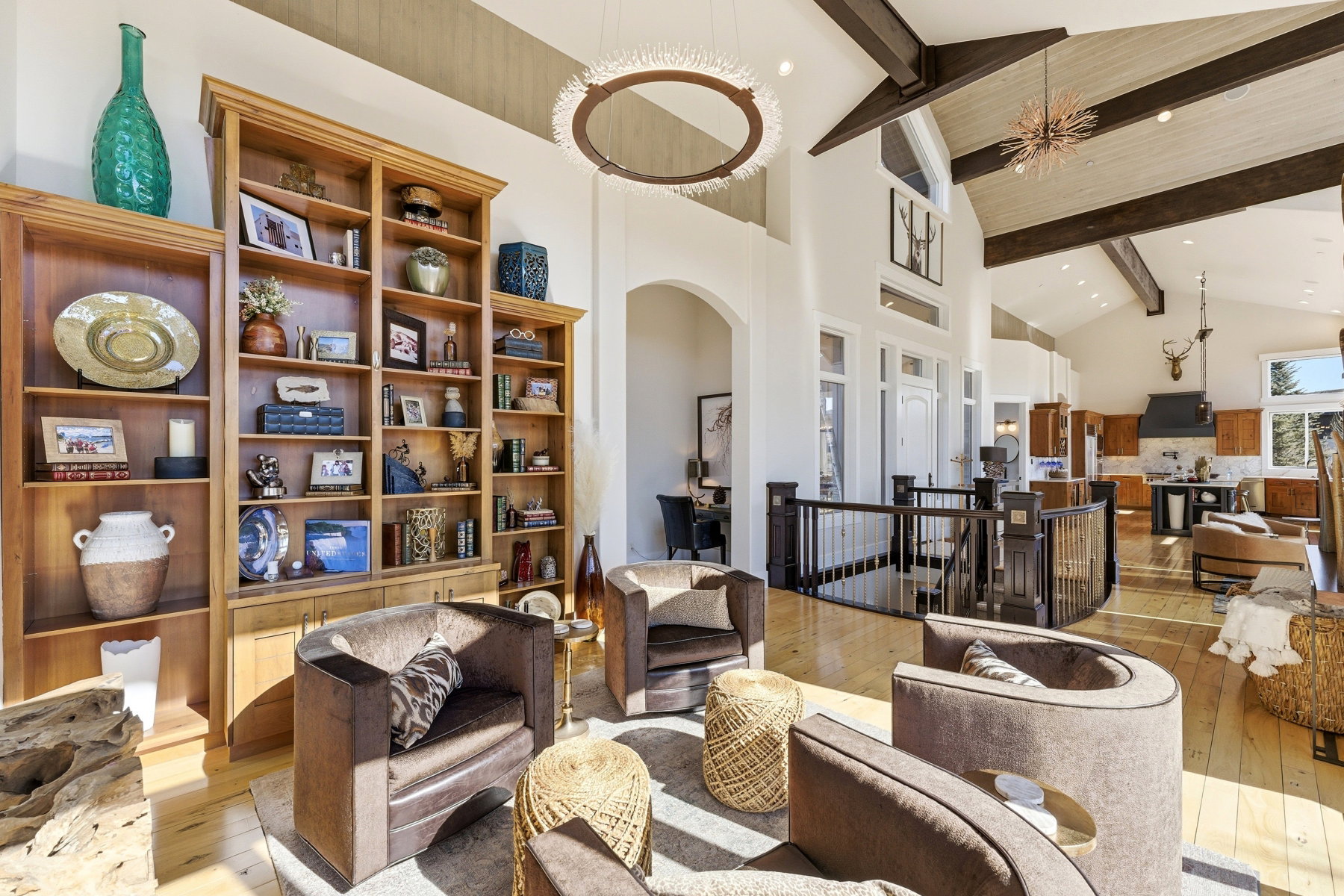 Spacious living area featuring high vaulted ceilings with exposed beams, light wood-finish flooring, and a grand built-in bookcase