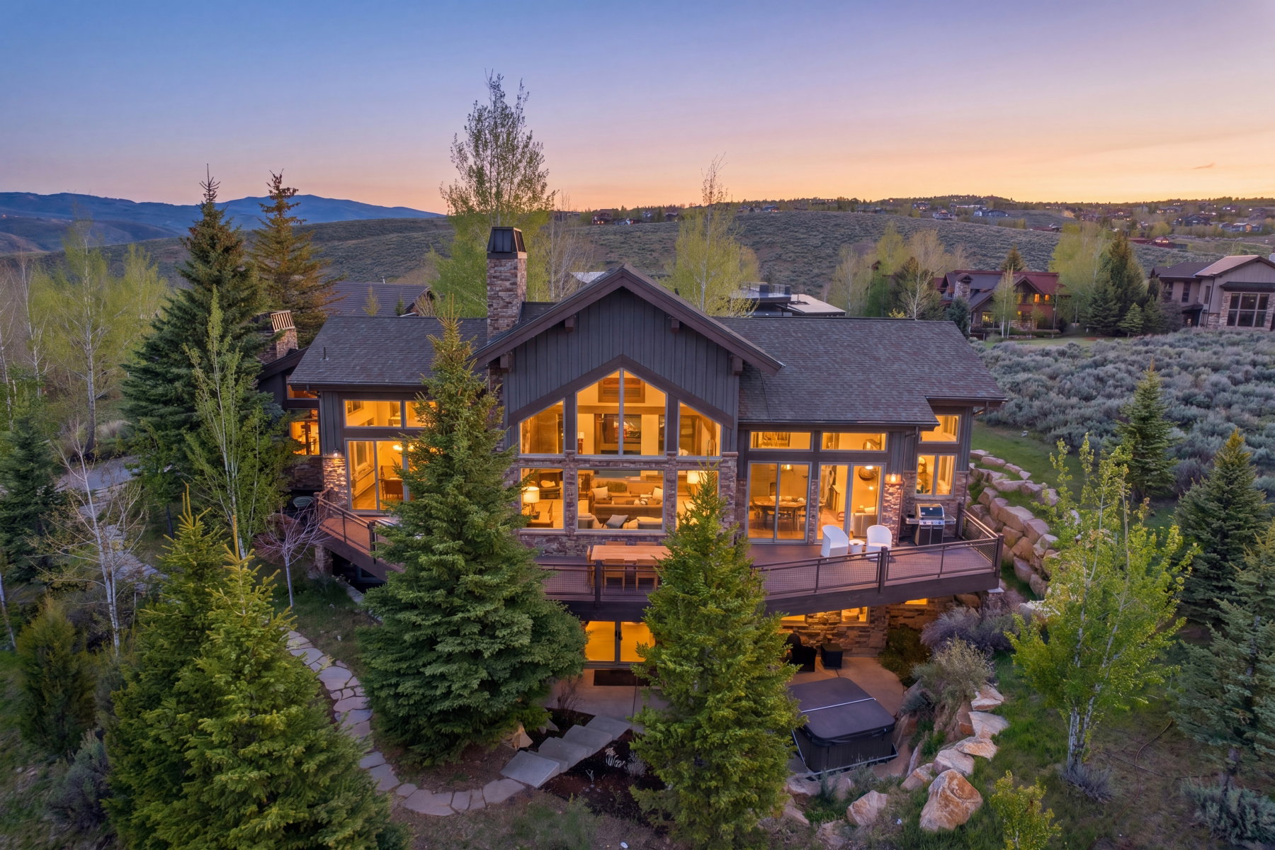 Mountain modern residence featuring extensive glazing, a stone chimney, and a multi-level deck