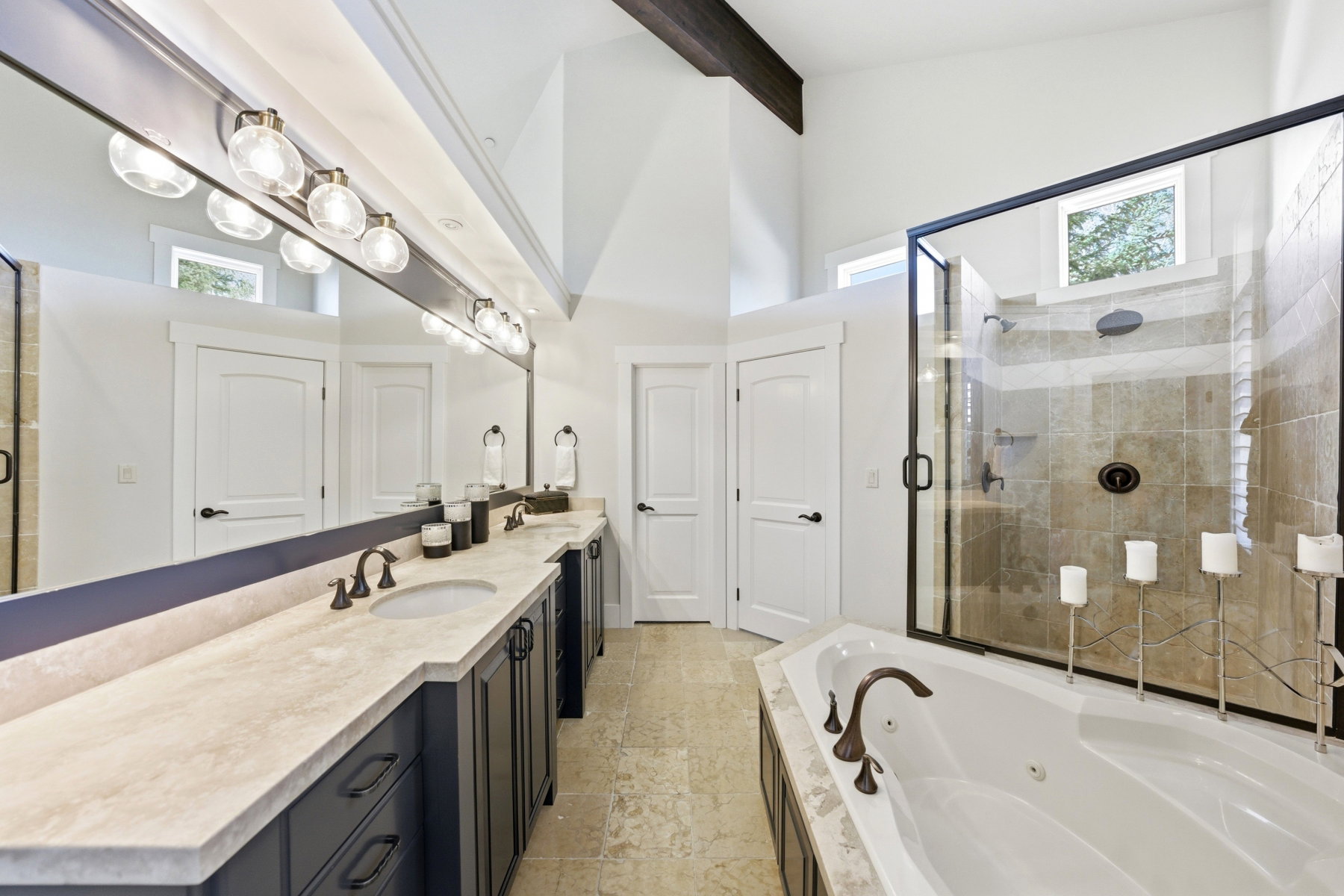 Spacious bathroom featuring a dual vanity with undermount sinks, a soaking tub with bronze fixtures, and a glass-enclosed shower with tiled walls