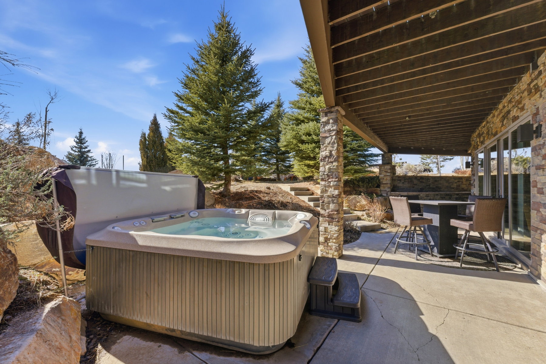 Outdoor patio featuring a built-in hot tub with cover, stone columns, a covered outdoor dining area, and large glass patio doors