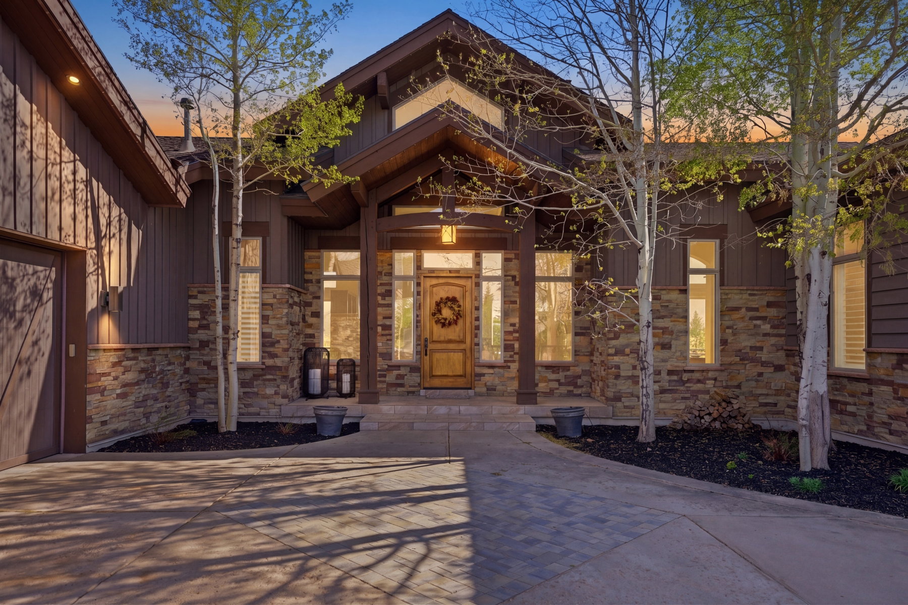 Craftsman-style exterior featuring vertical and horizontal siding, stone accents, a prominent covered entry, a paneled wood front door, and a paver stone driveway