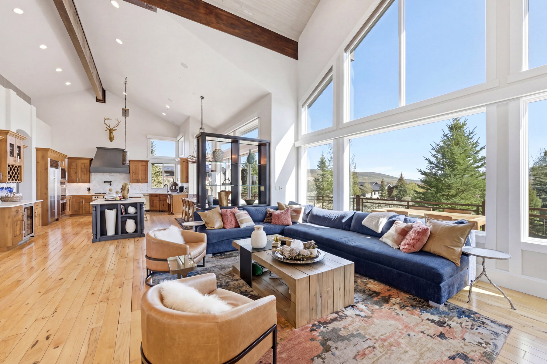 Great room featuring expansive windows, wood-finish flooring, vaulted ceilings with exposed beams, a central kitchen island, and a range hood
