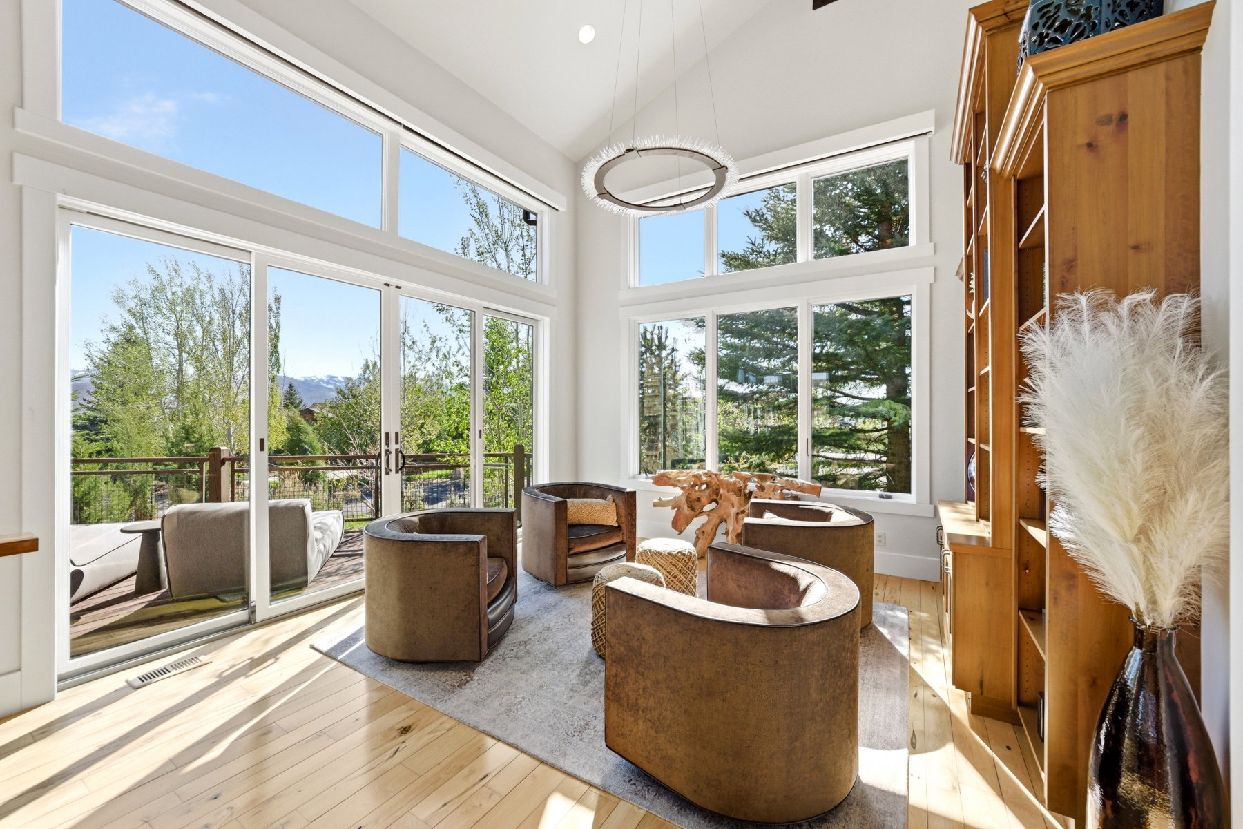 Living area featuring abundant natural light, vaulted ceilings, light wood-finish flooring, a contemporary chandelier, and a built-in wood bookcase