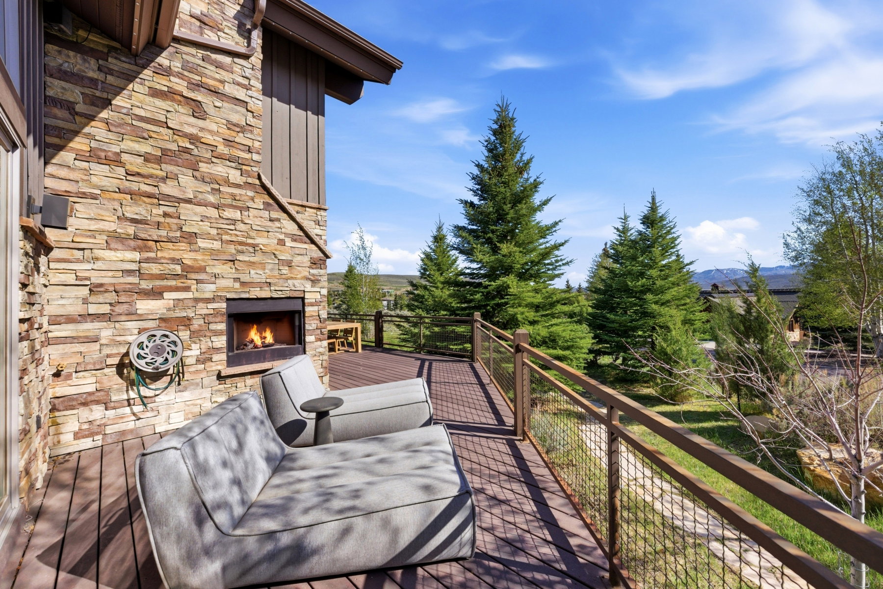 Expansive outdoor deck featuring wood-finish flooring, a stacked stone fireplace, and a metal railing system