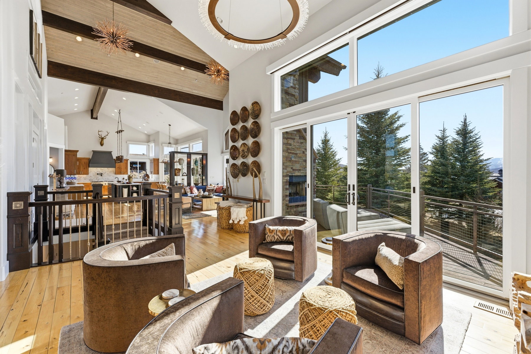 Spacious living area featuring floor-to-ceiling sliding glass doors, light wood-finish flooring, a vaulted ceiling with exposed beams, and a large circular chandelier