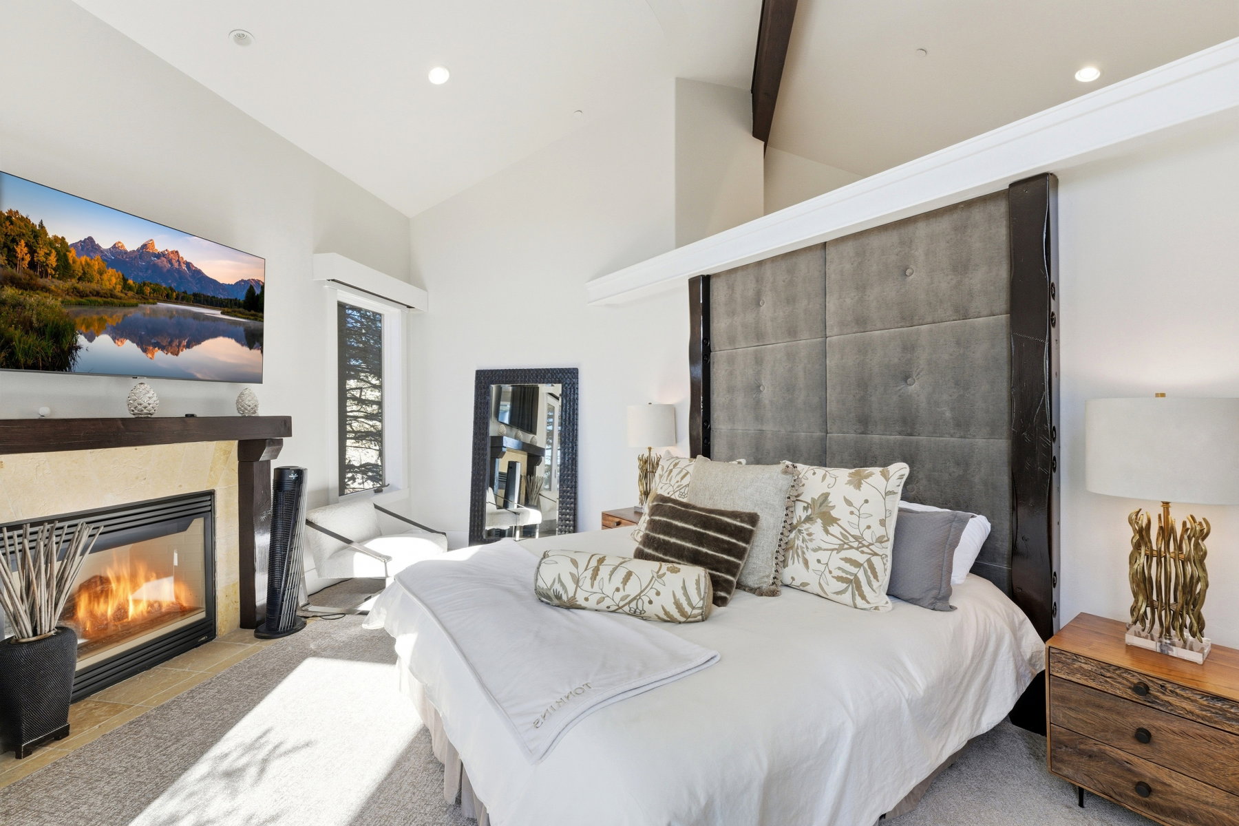 Bedroom featuring a vaulted ceiling with exposed wood beams, a stone-surround fireplace, and an oversized tufted headboard