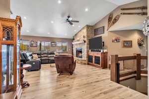 Living room with a ceiling fan, vaulted ceiling, light wood-style floors, a fireplace, and recessed lighting