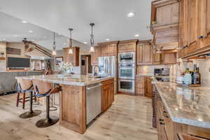 Kitchen featuring wood finish cabinets, open floor plan, a breakfast bar area, a center island with sink, and stainless steel appliances